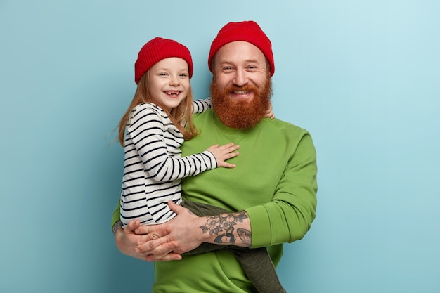 Homem com barba ruiva vestindo roupas coloridas e segurando a filha