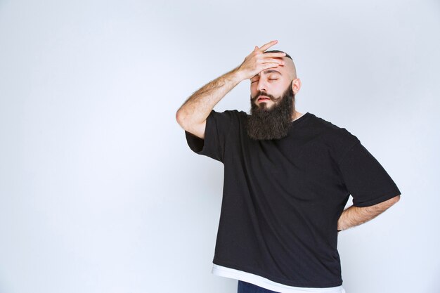 Homem com barba segurando a cabeça, pois ele tem dor de cabeça.