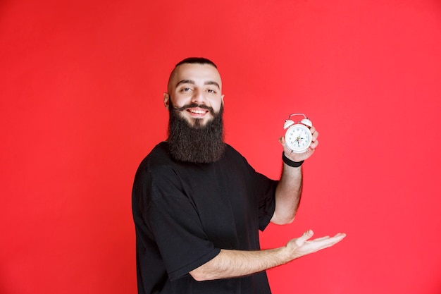 Homem com barba segurando e promovendo um despertador como um produto.