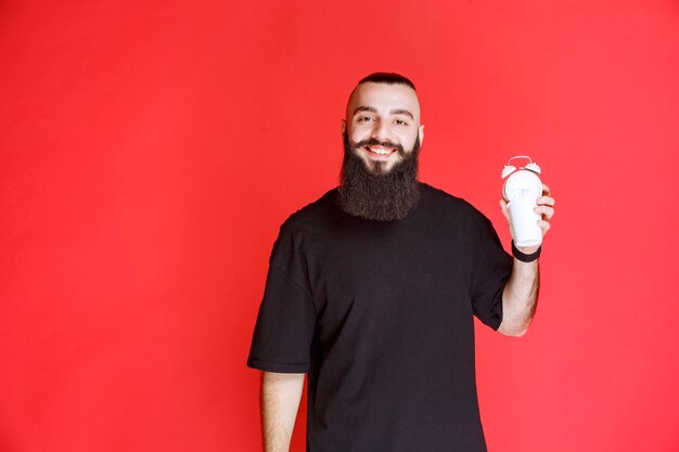 Homem com barba segurando e promovendo um despertador como um produto.