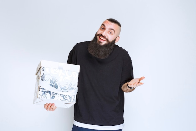 Homem com barba segurando uma caixa de presente azul branca, sorrindo e se sentindo feliz.