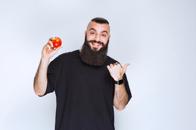 Homem com barba segurando uma maçã vermelha ou pêssego e apreciando o sabor.