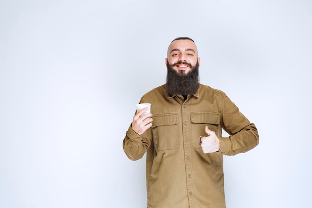 Homem com barba segurando uma xícara de café e apreciando o sabor.