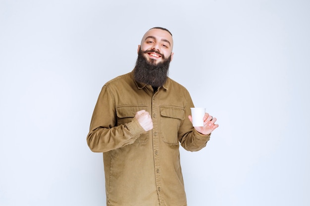 Homem com barba segurando uma xícara de café e apreciando o sabor.