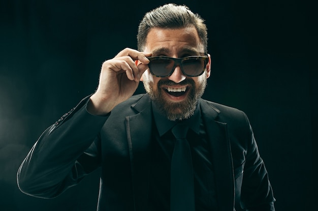 homem com bardo de terno. Homem de negócios elegante em fundo preto. Belo retrato masculino. Jovem emocional.