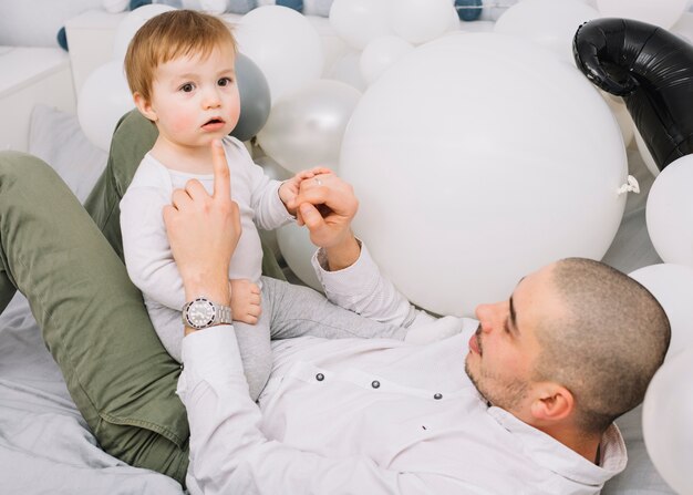 Homem com bebê brincando na cama perto de balões