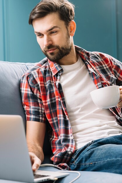 Homem, com, bebida, usando computador portátil