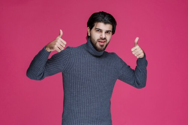 Homem com cabelo comprido e barba fazendo sinal de mão polegar para cima.