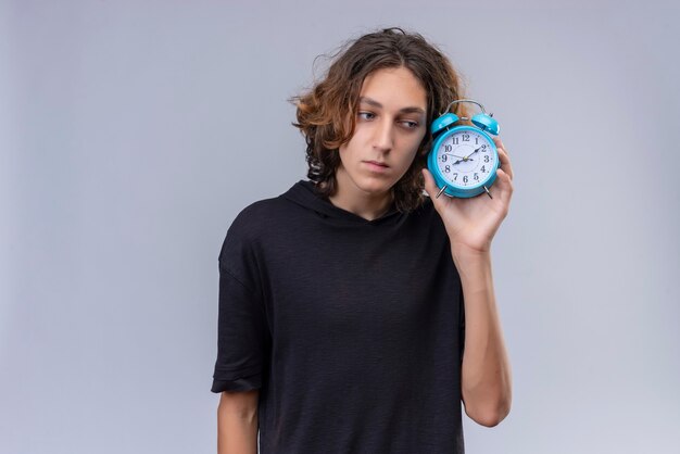 Homem com cabelo comprido e camiseta preta segurando um despertador