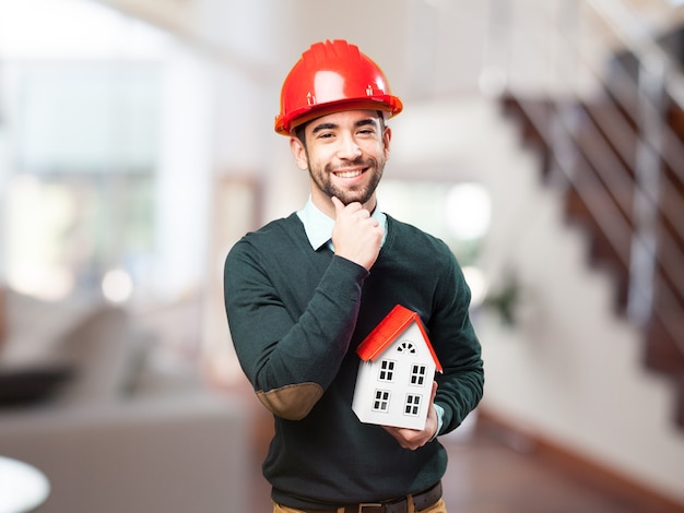 Homem com capacete vermelho e uma pequena casa na mão