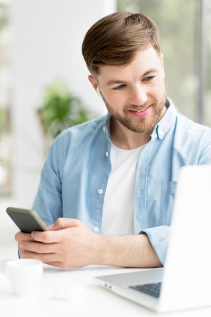 Homem com celular olhando no laptop