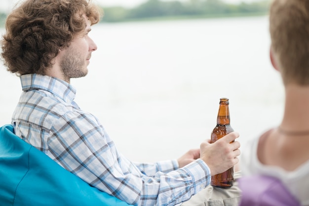 Foto grátis homem com cerveja relaxante perto do rio e amigo