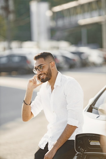 Foto grátis homem com conversa móvel enquanto espera o carro elétrico. estação de recarga, carros ecológicos.