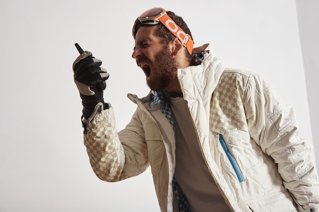 Homem com equipamento de snowboard e óculos na cabeça gritando no walkie talkie