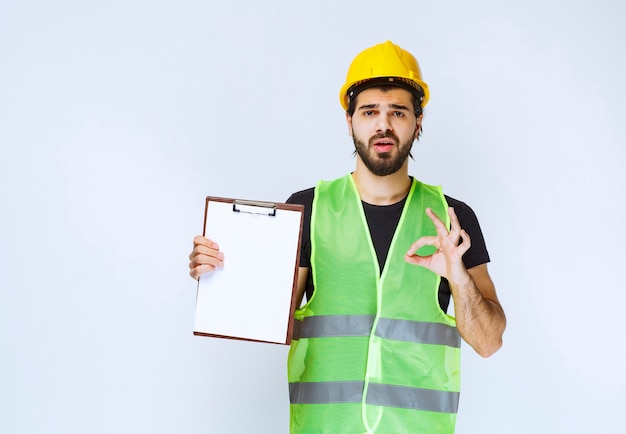 Homem com equipamento segurando a pasta do projeto e mostrando sinal de satisfação.