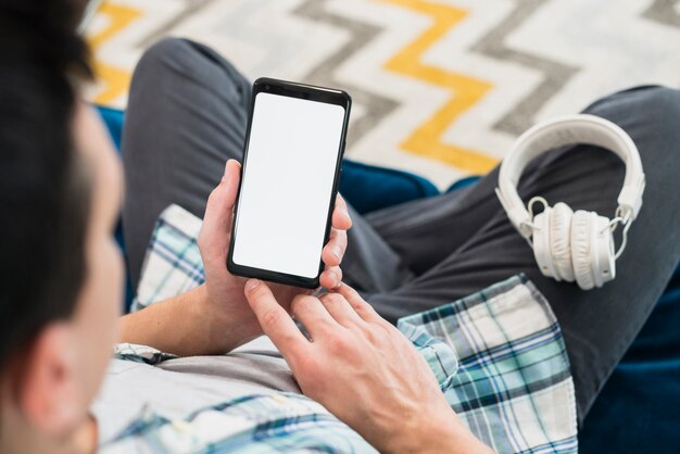 Homem com fones de ouvido na perna usando smartphone no sofá