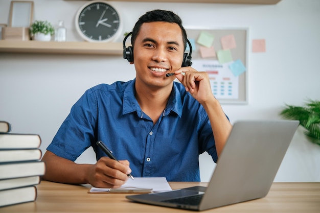 Homem com fones de ouvido trabalhando no escritório com papéis e laptop na mesa