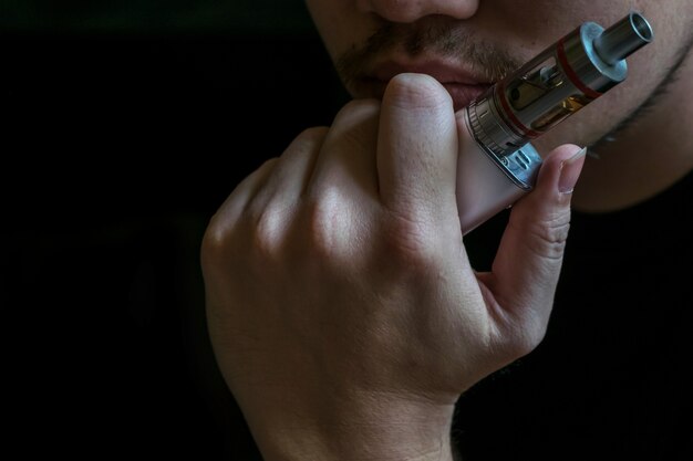 Homem com identidade escondida fumando um polêmico vaping e um cigarro eletrônico. Vaping é discutível na comunidade de saúde se for seguro ou um risco para a saúde