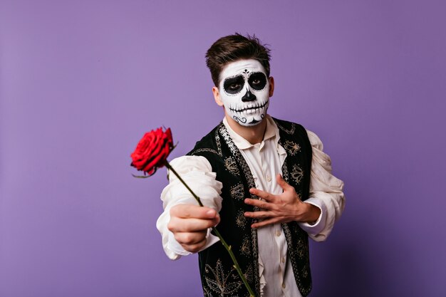 homem com maquiagem de morto mexicano segurando flor vermelha. cara emocional em roupas tradicionais espanholas.