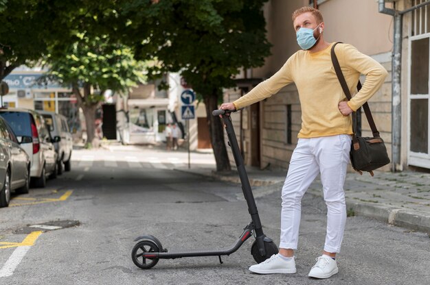 Homem com máscara médica segurando sua scooter