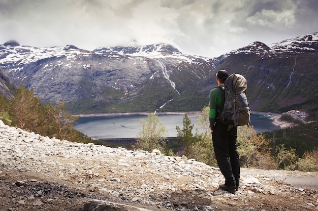 Homem com mochila turística fica diante da linda vista nas montanhas da Noruega