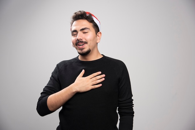 Homem com os olhos fechados com chapéu vermelho de Papai Noel colocou as mãos no coração.