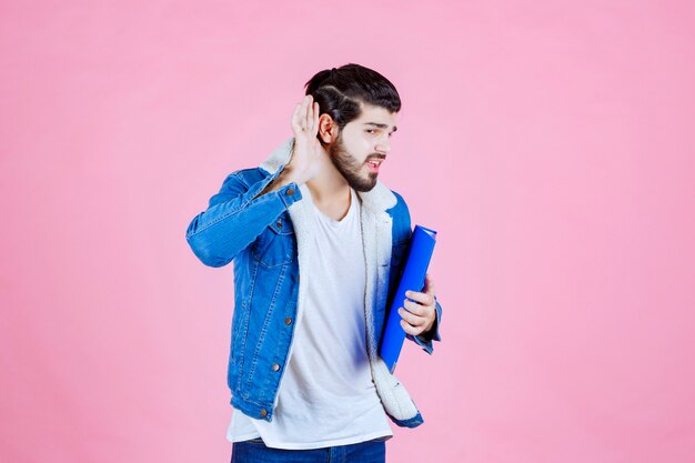 Homem com pasta azul apontando para a orelha, pois não ouve bem