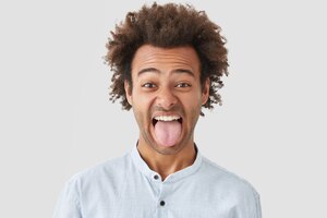 Homem com penteado afro mostra língua ao perceber algo nojento, faz careta, demonstra caráter teimoso