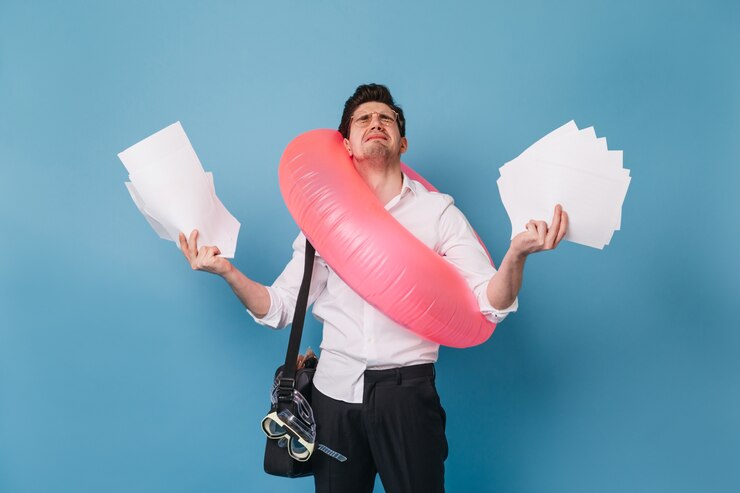 Foto grátis homem com roupa de escritório chora, segurando muitas folhas de papel. cara quer sair de férias e posando com um círculo inflável no espaço azul.