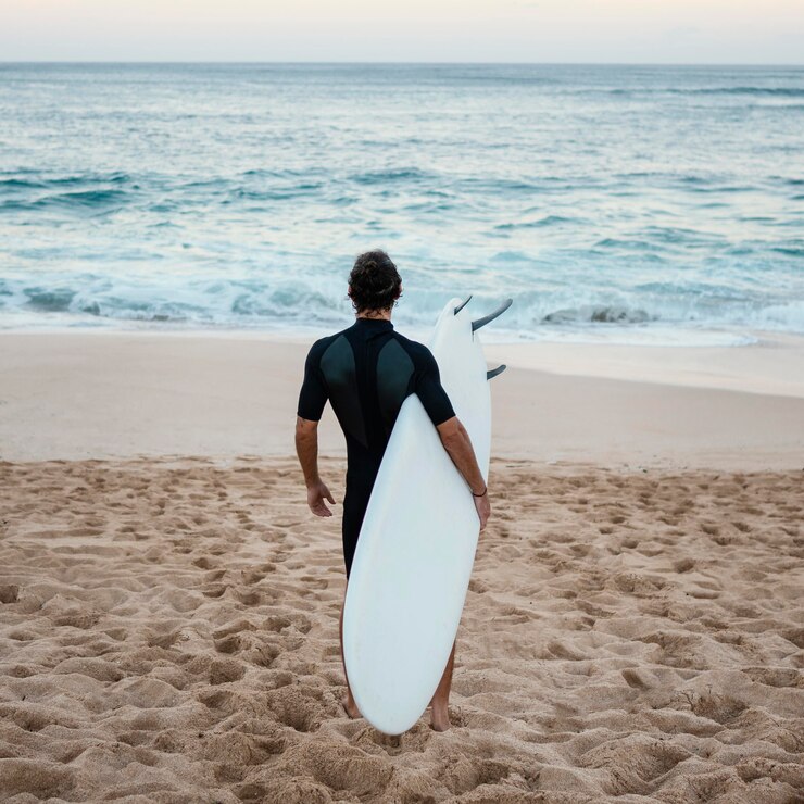 Foto grátis homem com roupa de surfista caminhando na areia por trás