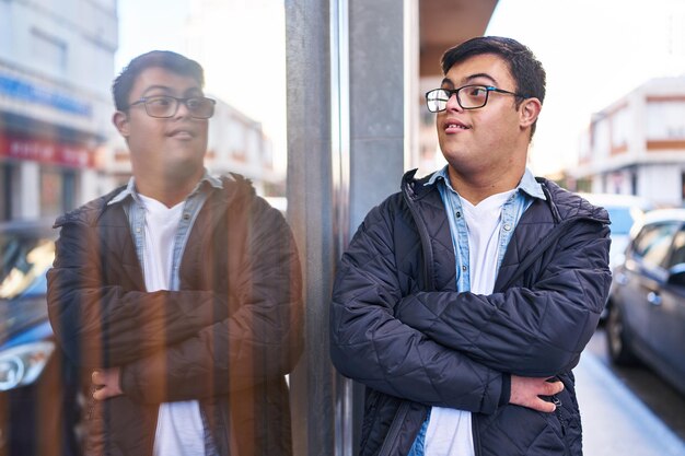 Foto grátis homem com síndrome de down sorrindo confiantemente de pé com os braços cruzados gesto na rua