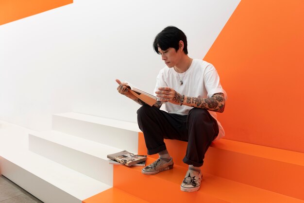 Homem com tatuagens, bebendo café e lendo um livro em um café