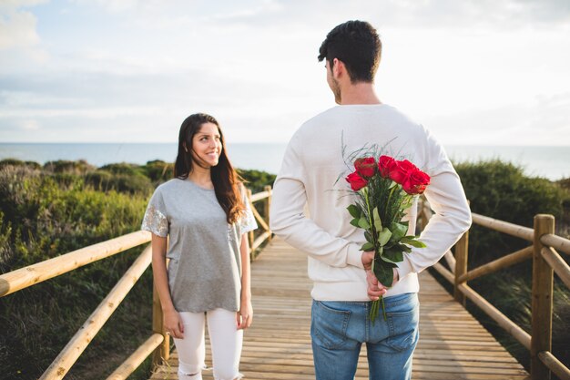 Homem com um buquê de rosas nas costas olhando para sua namorada