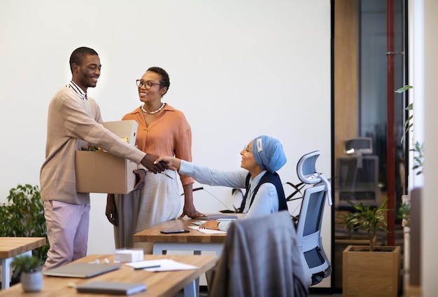 Homem com uma caixa de pertences sendo apresentado aos colegas de trabalho em seu novo emprego