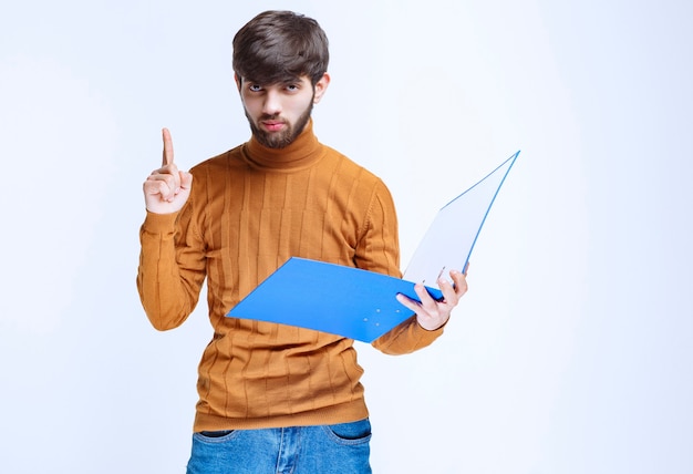 Homem com uma pasta azul, levantando o dedo para chamar a atenção. h