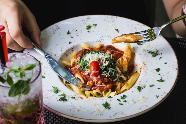 Homem comendo macarrão penne à bolonhesa, guarnecido com ervas