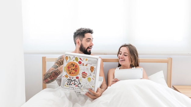 Homem comendo pizza enquanto sua esposa usando tablet digital