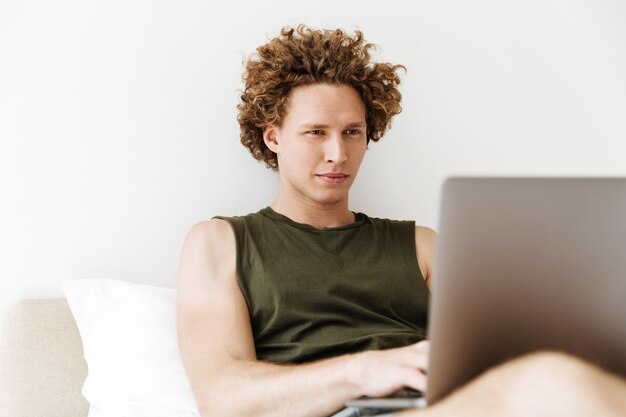 Homem concentrado encontra-se na cama em casa usando laptop