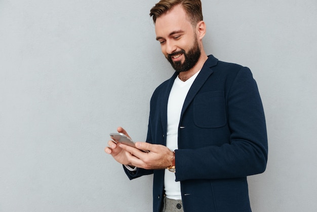 Homem concentrado sorridente usando smartphone isolado sobre cinza