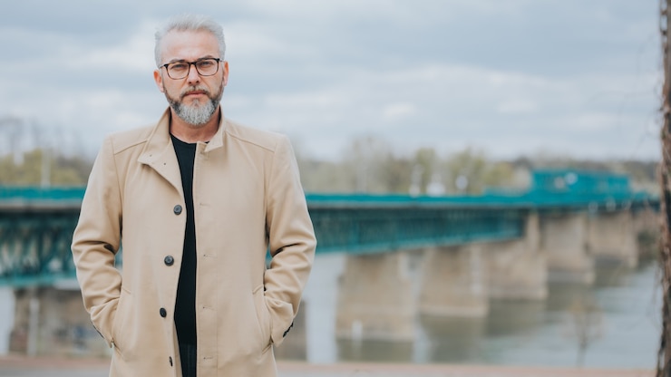Foto grátis homem confiante com cabelos grisalhos, vestindo um elegante casaco marrom com uma ponte atrás