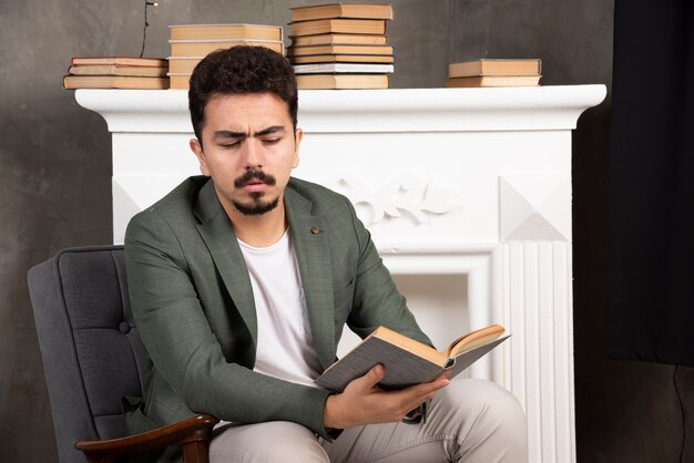 Homem confiante de handsime lendo livro em um sofá.