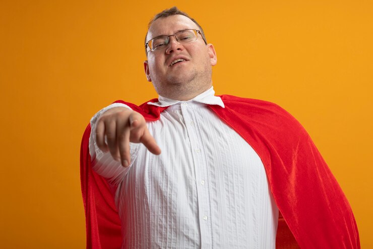 Foto grátis homem confiante super-herói eslavo adulto com capa vermelha e óculos, olhando e apontando isolado na parede laranja