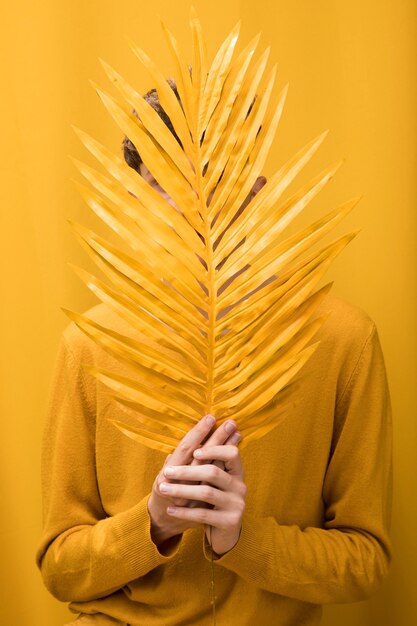 Homem considerável novo atrás da folha de palmeira em uma cena amarela