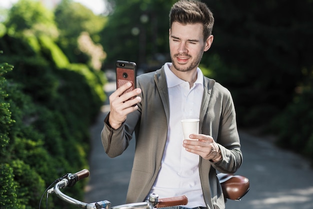 Homem considerável novo que está com a bicicleta que toma o selfie no telefone celular