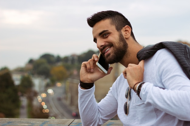 Homem considerável que fala no telefone ao ar livre. Com jaqueta de couro, óculos de sol, um cara com barba. Efeito Instagram