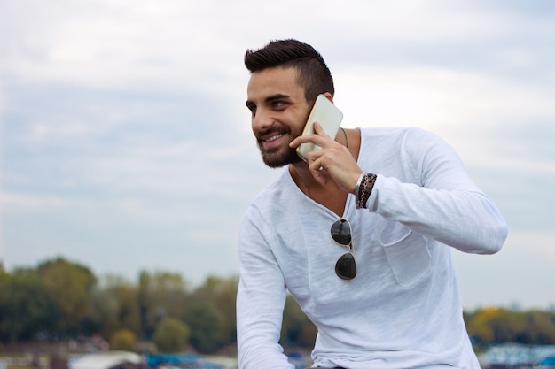 Homem considerável que fala no telefone ao ar livre. Com jaqueta de couro, óculos de sol, um cara com barba. Efeito Instagram