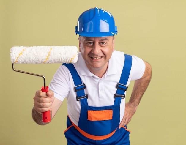 Foto grátis homem construtor adulto e sorridente, de uniforme, segurando uma escova giratória sobre verde oliva