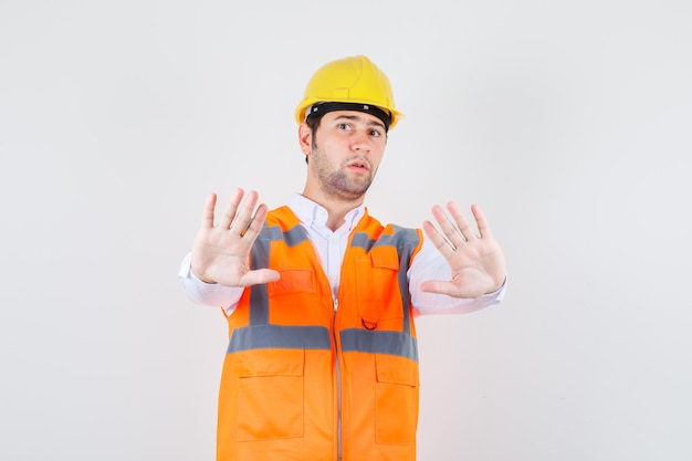 Homem Construtor mostrando bastante gesto na camisa, uniforme e olhando sério. vista frontal.