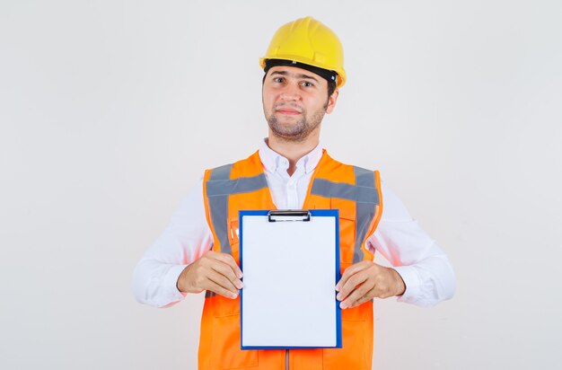 Homem Construtor segurando a prancheta e sorrindo de camisa, uniforme, vista frontal.