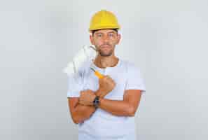 Foto grátis homem construtor segurando rolo de pintura em t-shirt branca, capacete e olhando confiante, vista frontal.